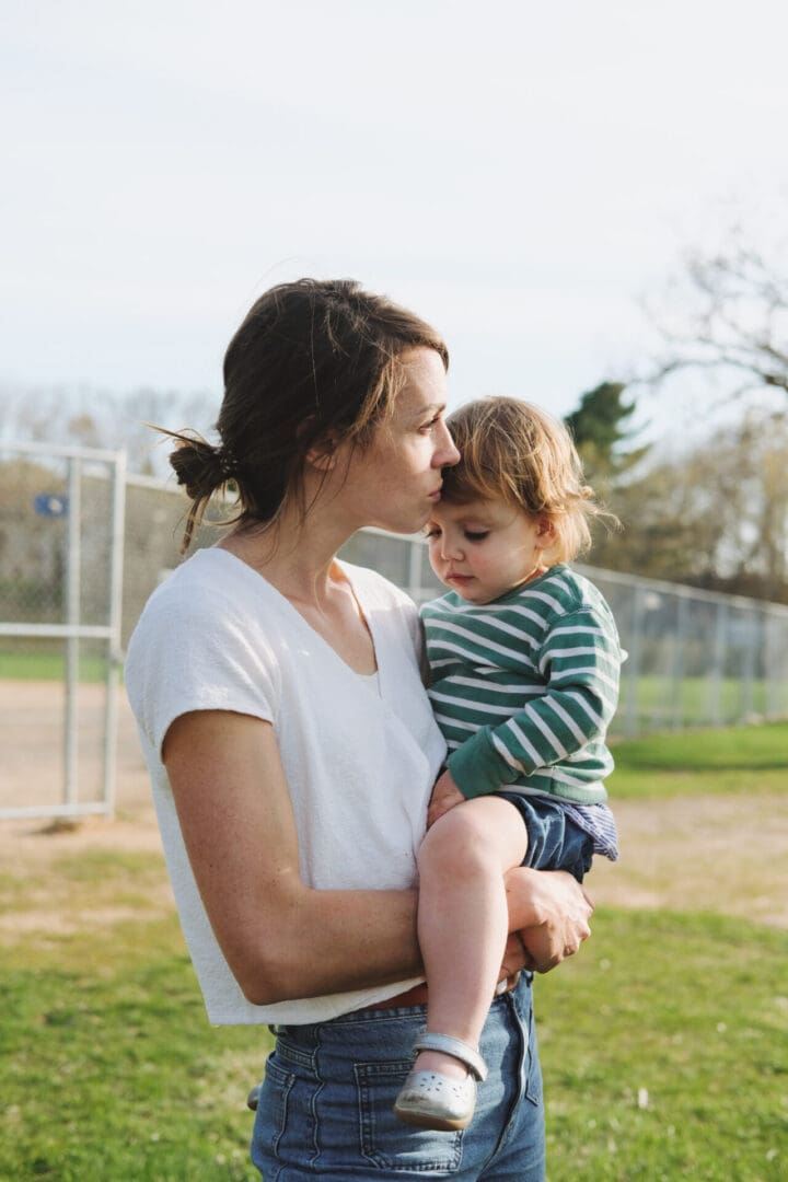 Beth holding Willa at baseball diamond Well-Read Mom