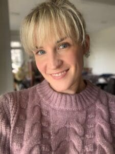 A woman, in a purple sweater, smiles for the camera.