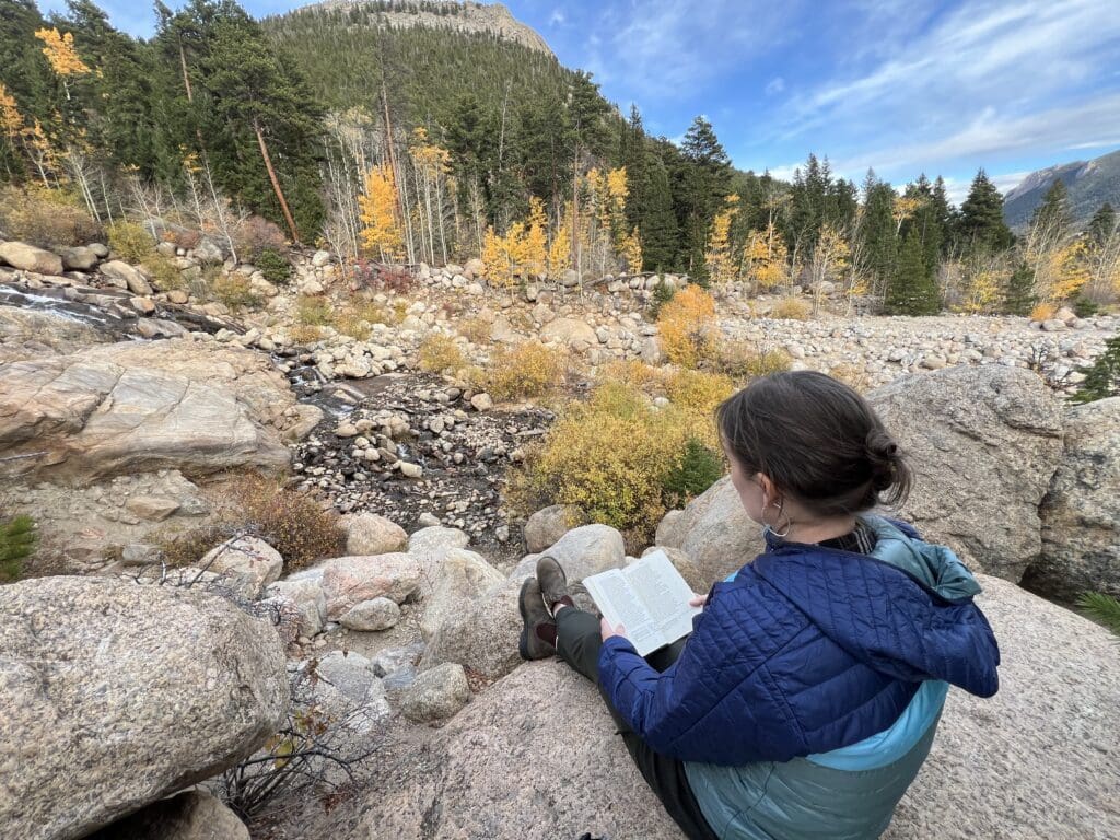 Person reading on rocks in mountainous landscape.