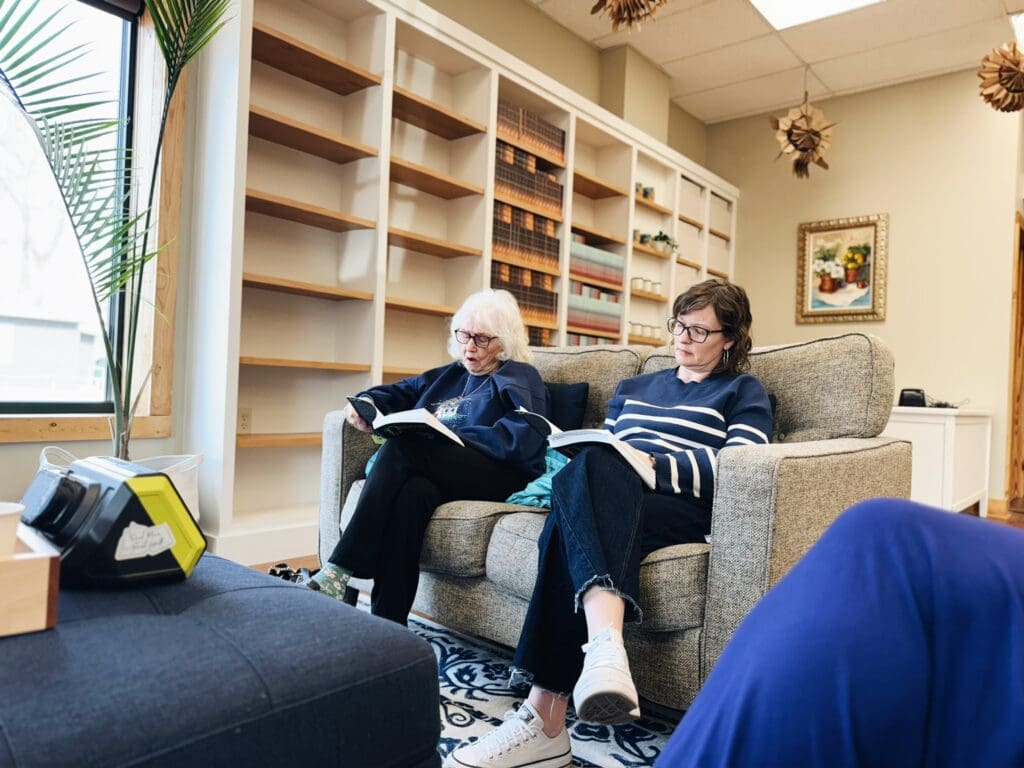 Two people sitting on a couch in a cozy living room with shelves in the background.