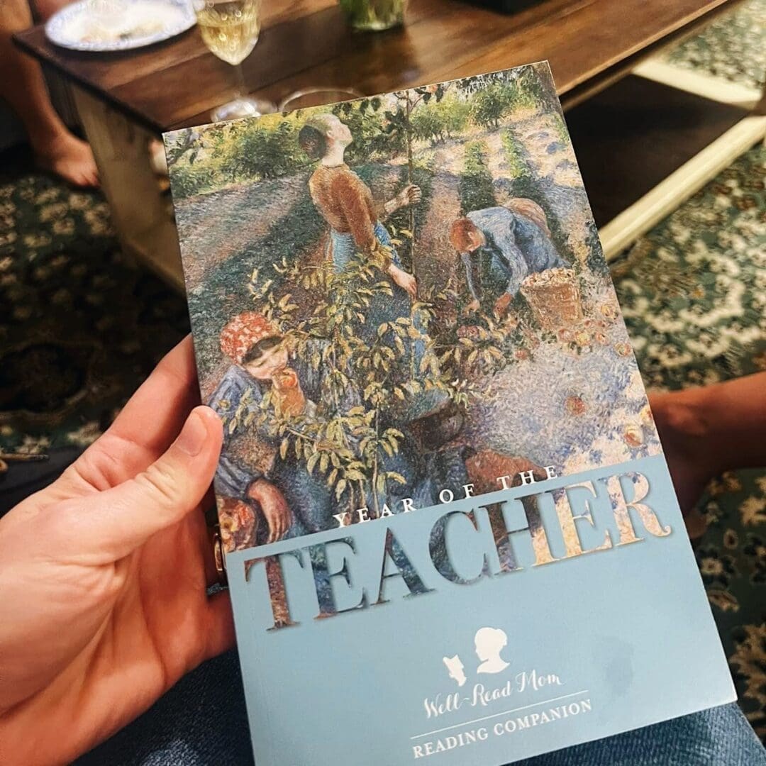 A person holding a 'Teacher' themed calendar featuring an artistic painting.