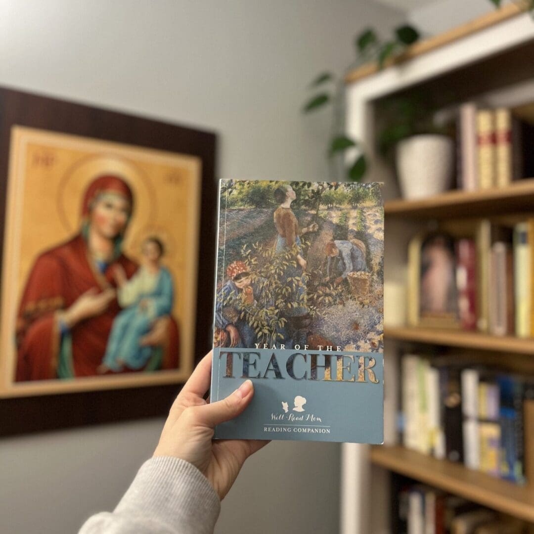 A person holds up the book 'Peace' in a cozy room with bookshelves and religious art.